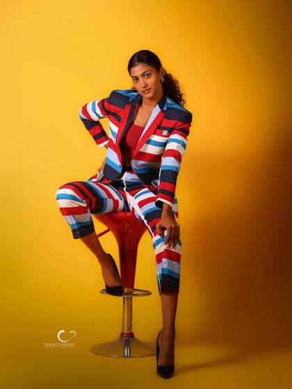 A confident and powerful pose on a red stool, which adds another pop of color. This shot is a celebration of bold fashion and fearless attitude.