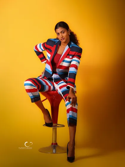 A confident and powerful pose on a red stool, which adds another pop of color. This shot is a celebration of bold fashion and fearless attitude.