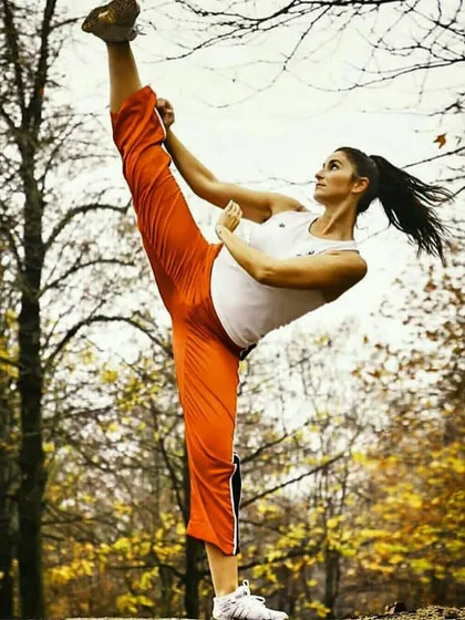 A student performs a high kick in an outdoor setting, showing the grace and power that comes from consistent practice.