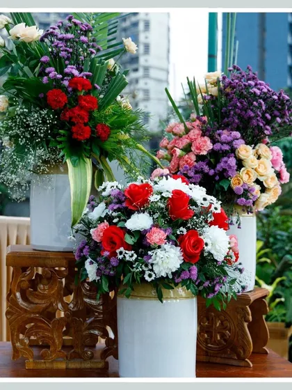 A trio of stunning floral centerpieces, combining roses, carnations, and asters in white vases, adding vibrant color and elegance to the event space.