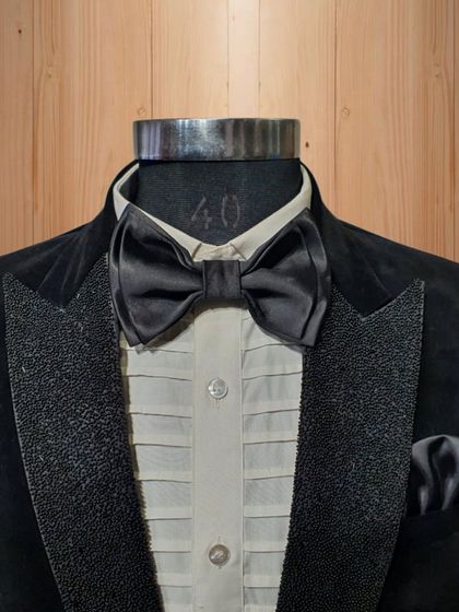 A close-up on the details of the black velvet tuxedo. The textured lapel and satin bow tie show the interplay of different materials to create a sophisticated and tactile garment.