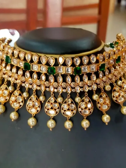 A product shot of a beautiful Kundan choker with green stones and pearl drops. This is a versatile piece that can be styled in many ways.