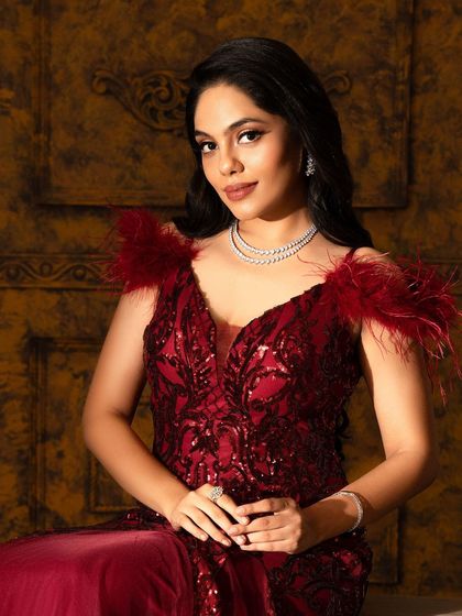 This deep red gown is all about drama and romance. The bodice features intricate sequin work, while the feather-adorned shoulders and flowing tulle skirt add a touch of old Hollywood glamour.
