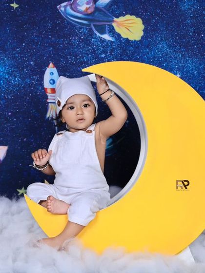 A little explorer adjusts his astronaut helmet while sitting on the moon. This space-themed photoshoot is a unique and creative way to celebrate a milestone.