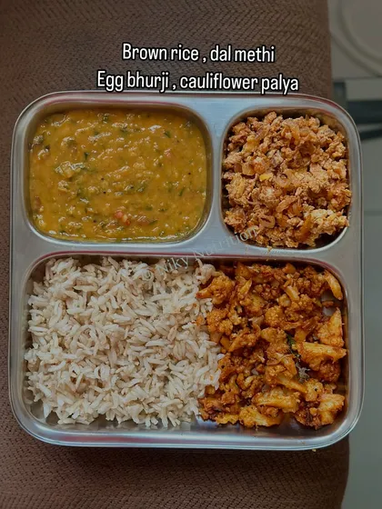 A balanced non-vegetarian meal of brown rice, dal methi, egg bhurji, and cauliflower palya. It provides a good mix of protein, carbs, and vegetables.