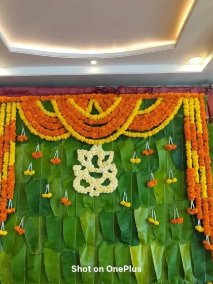 A close-up of the banana leaf and marigold backdrop for a baby shower. The Ganesha motif made from white flowers adds a divine and auspicious element to the decor.