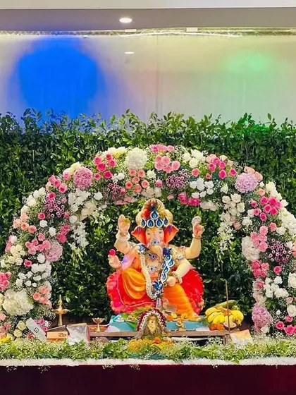 A fresh floral arch in shades of pink and white over a green leaf backdrop. This design provides a beautiful, garden-like setting for the Ganpati idol, enhanced with soft colored lighting.