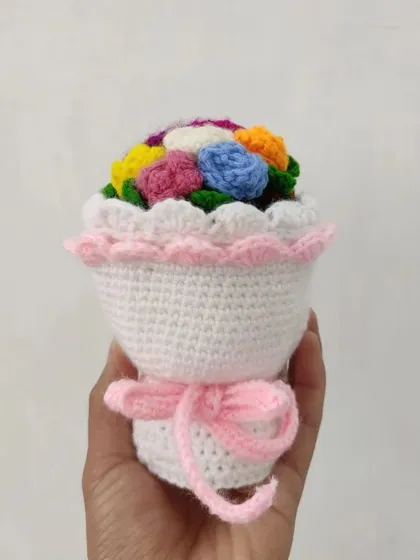 A miniature crochet bouquet featuring a rainbow of small flowers, held in a white crocheted wrap with a pink ribbon. These are perfect as a small, thoughtful gift.