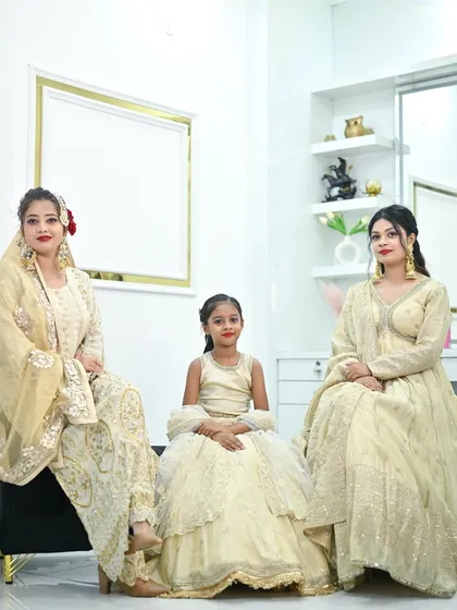 A beautiful family portrait featuring coordinated ivory and gold outfits. The collection includes a sharara set, an anarkali, and a matching kids' lehenga.