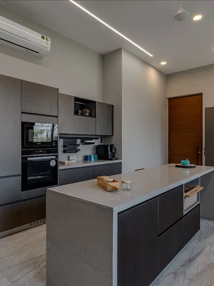 The combination of dark metallic cabinets and a glossy black refrigerator creates a sleek, high-tech look, balanced by the natural light from the window.
