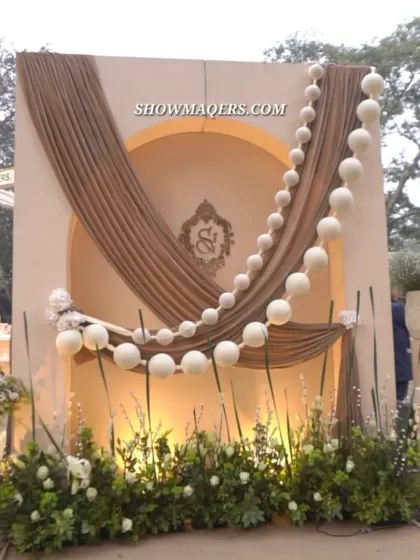 A personalized photo backdrop for the couple, featuring their monogram, draped fabric, and a beautiful garland of white pom poms.