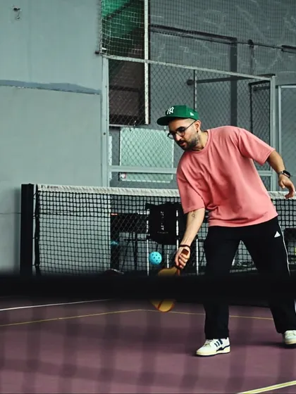 A player lunges for a low shot at the net during a pickleball game. The purple court and indoor setting ensure a perfect game, day or night.
