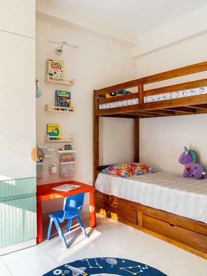 This kids' room is bright and cheerful, with a classic wooden bunk bed that includes storage drawers underneath. A small study desk and open shelving for books make it a complete and functional space for learning and play.