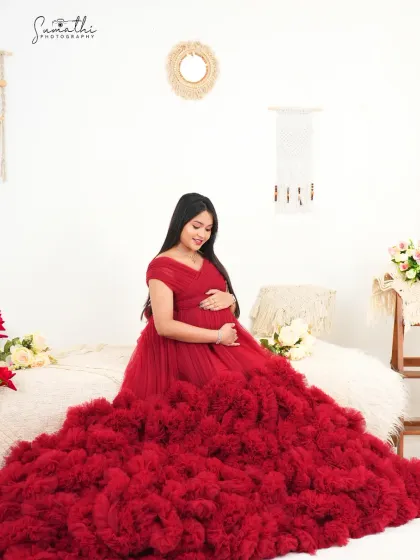 A full-length portrait of a mother-to-be in a stunning red ruffled gown against a boho backdrop. The combination of bold color and soft textures creates a unique and stylish look.