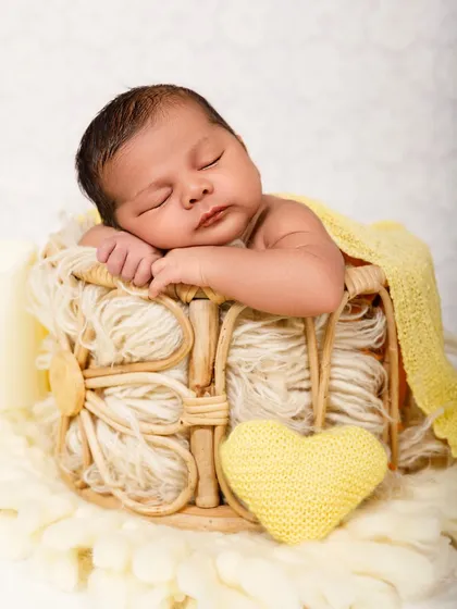 Another angle of a peaceful newborn sleeping in a basket, with a yellow heart prop adding a touch of sweetness.