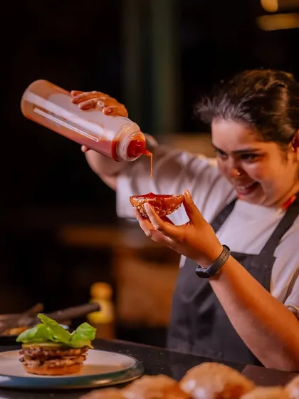 A chef adds a generous squeeze of Harissa, a peppery, smoky sauce that is the perfect companion to our gourmet burgers.