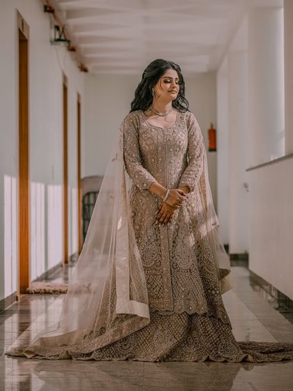 A full-length portrait of a bride in an elegant, floor-length gown, captured in a well-lit corridor.
