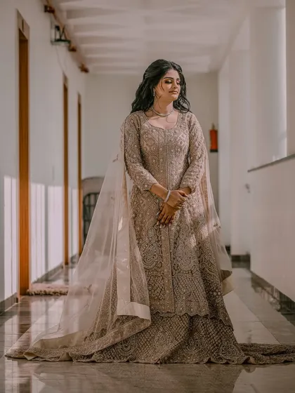 A full-length portrait of a bride in an elegant, floor-length gown, captured in a well-lit corridor.