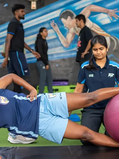 A physiotherapist supervises an athlete performing a side plank with a stability ball. This exercise challenges core strength and hip stability, crucial components of our integrated approach to rehabilitation and performance.