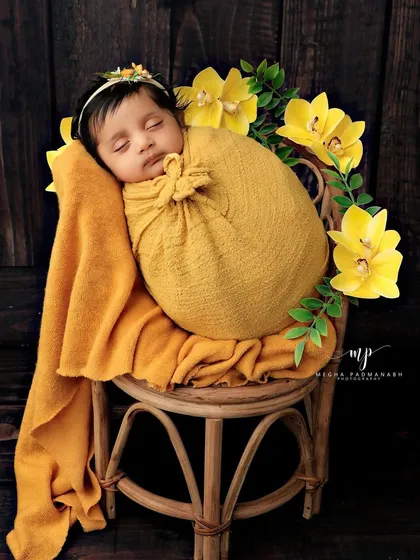 A slightly different angle of the baby on the rattan chair, surrounded by yellow flowers.