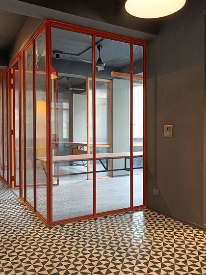 For an upcoming New Delhi office, we used bold red-framed glass partitions to define meeting rooms within a monochromatic envelope, set against a striking geometric tiled floor.