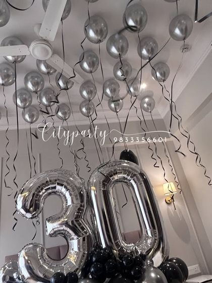 An upward-looking shot that emphasizes the effect of the silver balloons covering the ceiling, each with a hanging black ribbon, creating a festive party atmosphere.