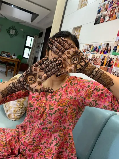 A playful shot of a happy client showing off her engagement mehndi. The design includes the couple's initials inside beautiful mandalas on her palms.