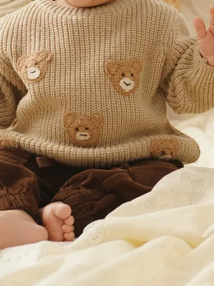 A close-up on the adorable details of a baby's outfit, featuring a knit sweater with teddy bear patches, perfect for a themed birthday shoot.