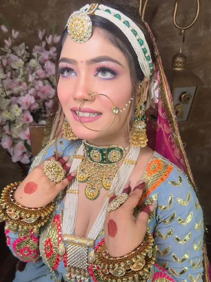 A smiling bride wearing a traditional Rajasthani bridal set with a borla, nath, and layered necklaces. The colorful outfit is perfectly complemented by the gold and green jewellery.