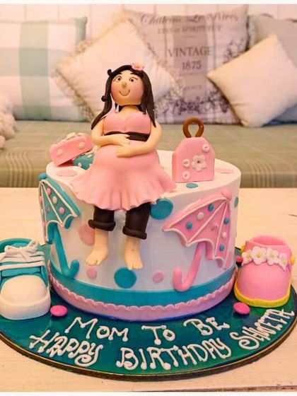 A sweet "Mom to Be" birthday cake, celebrating a baby shower with cute fondant shoes and umbrellas.