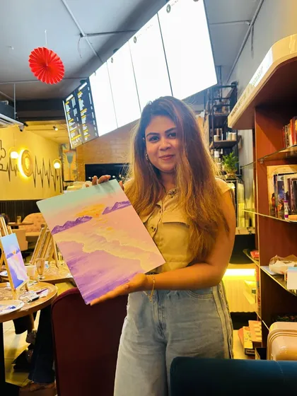 A participant proudly displaying her finished abstract beach painting in a cafe.