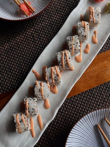A beautifully plated sushi roll drizzled with our signature spicy mayo. The roll is coated in sesame seeds, adding a nutty flavor and a bit of texture to every bite.