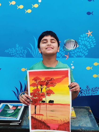 The pride on his face is priceless. This student is thrilled with his colourful painting of elephants at sunset.