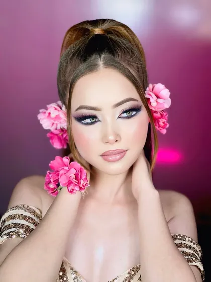 A portrait against a pink background. The lighting enhances the doll-like features and the vibrant colors of the makeup.