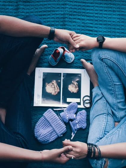 Two hearts, one bond, and a tiny heartbeat joining the rhythm. This top-down shot with ultrasound prints and baby shoes tells a beautiful story of new beginnings.