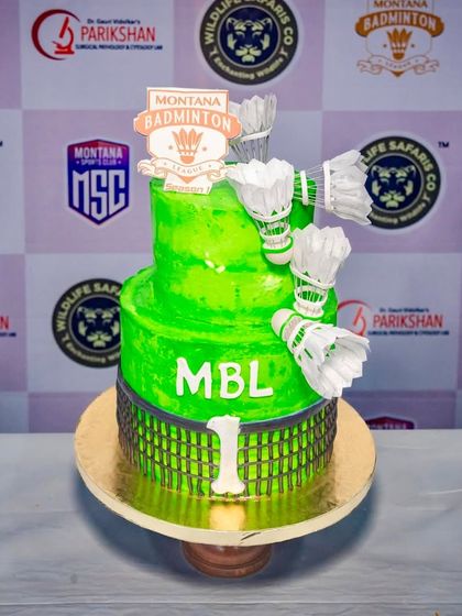 A sporty two-tier cake for the Montana Badminton League. The cake is vibrant green and decorated with a badminton net design and edible shuttlecocks, perfect for celebrating a tournament.