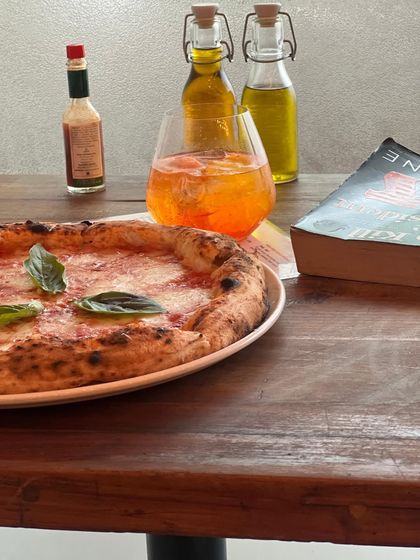 The perfect table setup: a Margherita pizza, a spritz, a good book, and our house-made infused oils.