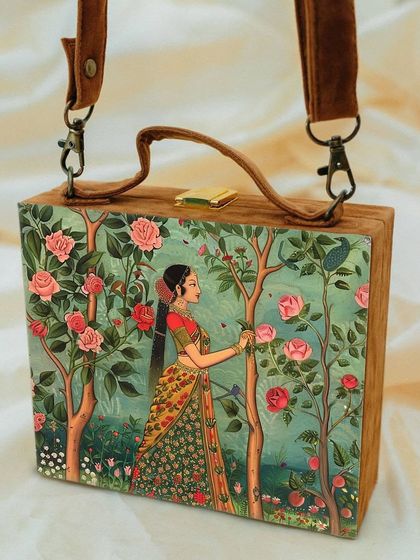 This suitcase-style bag features a serene traditional art print of a lady in a rose garden. The soft colors and detailed artwork on matte satin create a very elegant and classic look.