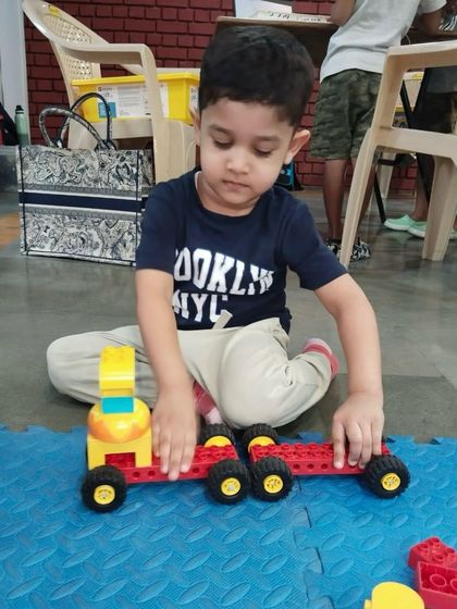 Building a vehicle with large LEGO pieces, this young student is learning about structure, wheels, and axles. My classes make learning fundamental engineering concepts fun.
