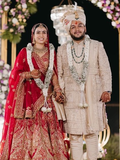 A classic portrait of the bride and groom. Her traditional red lehenga is paired with timeless makeup, featuring defined eyes and a warm, flattering lip color.
