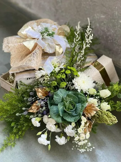 A lush and verdant gift hamper, where the packaging is as beautiful as the gift itself. This arrangement is defined by its exquisite floral design, using a mix of fresh greens and white flowers to create a natural, organic feel.