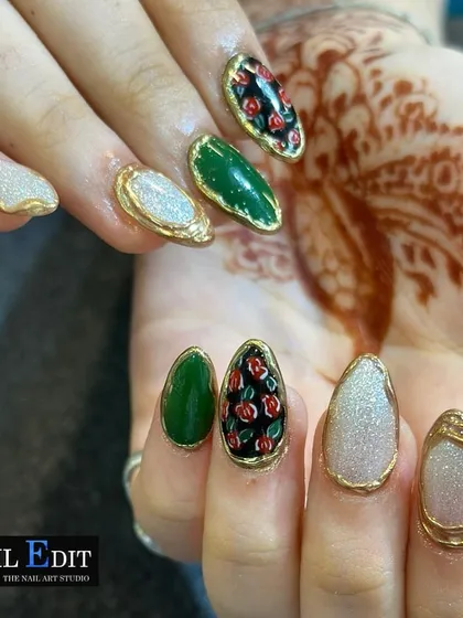 This luxurious set features jewel-like nail art with raised gold chrome borders. The designs include a solid emerald green, a glittery white, and a detailed hand-painted rose pattern on a black background, creating the look of ornate, framed miniature paintings.