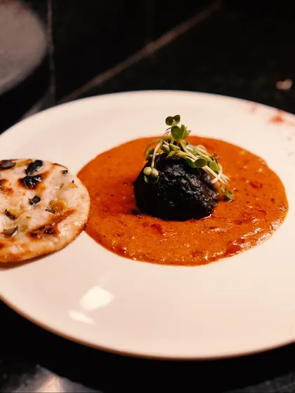A modern Indian creation where a rich, dark kofta is centered in a vibrant tomato gravy, served alongside a miniature naan. It's tradition, reimagined.