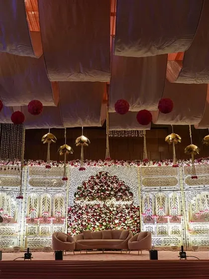 The main stage for a Sufi-inspired engagement, featuring a stunning backdrop of white jaali panels and a massive arch made of red and pink roses. The soft pink stage and sofas complete this romantic picture.