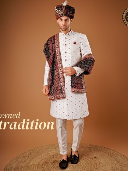Crowned in tradition. This complete groom's look features a white sherwani with a contrasting red and black stole and a matching safa, creating a powerful and regal statement.