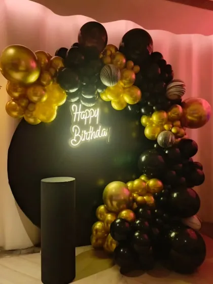 Here is a sleek and modern birthday decoration I did. The design uses a bold combination of black and chrome gold balloons around a circular black backdrop, with a 'Happy Birthday' neon sign providing a central focal point.