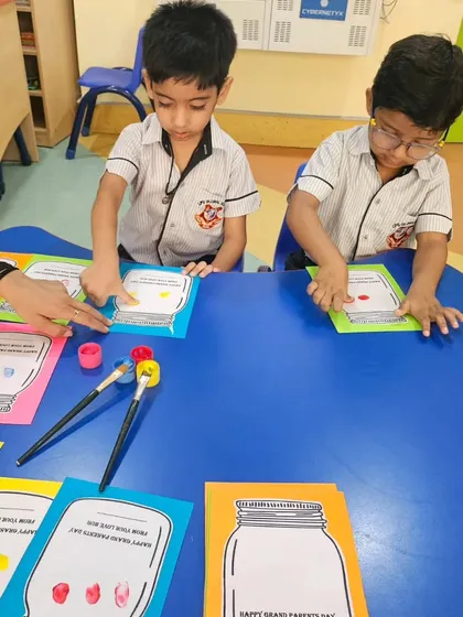 Two boys carefully dip their fingers in paint, fully engaged in the Grandparents Day craft activity.
