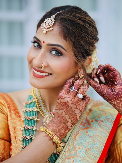 A candid moment of the bride adjusting her earring. This shot highlights the intricate henna design and the flawless finish of her makeup, even in an unposed moment.