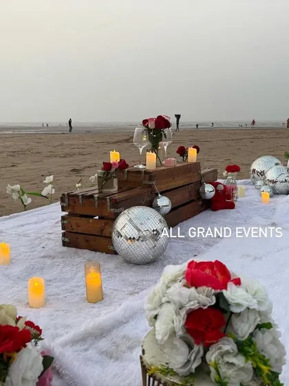 A dreamy beach proposal setup for a private and romantic moment by the sea. We arranged a comfortable picnic spot with a soft white blanket, a rustic table made from wooden crates, and decorated it with candles, flowers, and sparkling disco balls for a touch of fun.