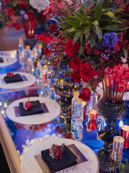 A beautifully styled tabletop with a mirrored surface reflecting the dramatic blue and red lighting, adorned with a single red rose on each plate.